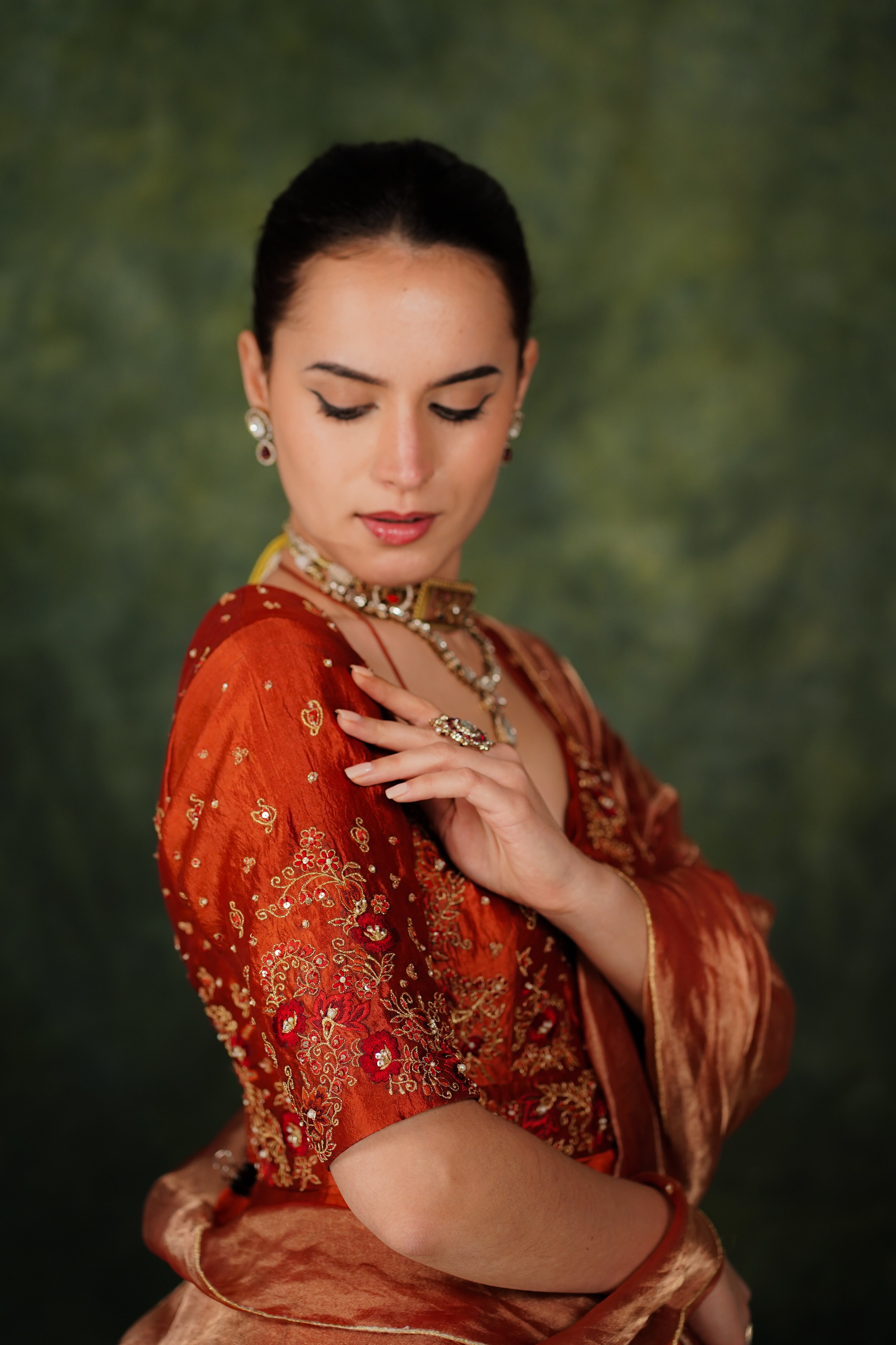 Woman in an orange traditional outfit with jewelry against a green background